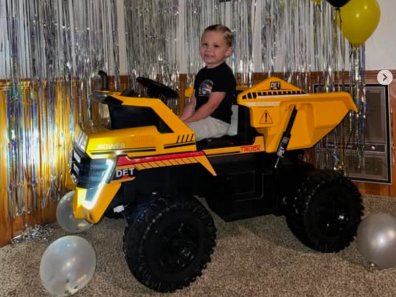 Birthday kid looking at camera and smiling while sitting on the Big Kahuna Dump Truck by Tough Trucks For Kids