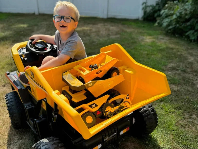 Kid looking at camera and smiling while hauling small CAT dump truck toys at the back of the Big Kahuna Dump Truck by Tough Trucks For Kids