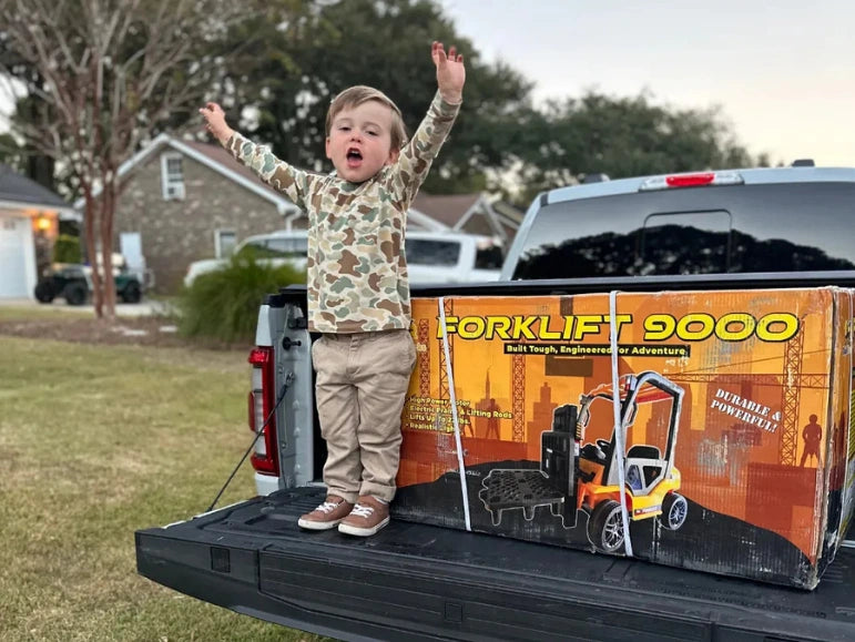 Kid celebrating standing on the truck door of a truck with the Forklift 9000 Box next to him